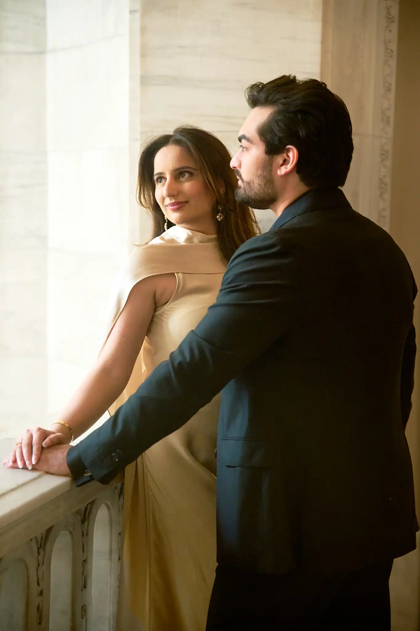Overhead intimate moment on a dim stairwell, his lips at her cheek in warm tungsten light