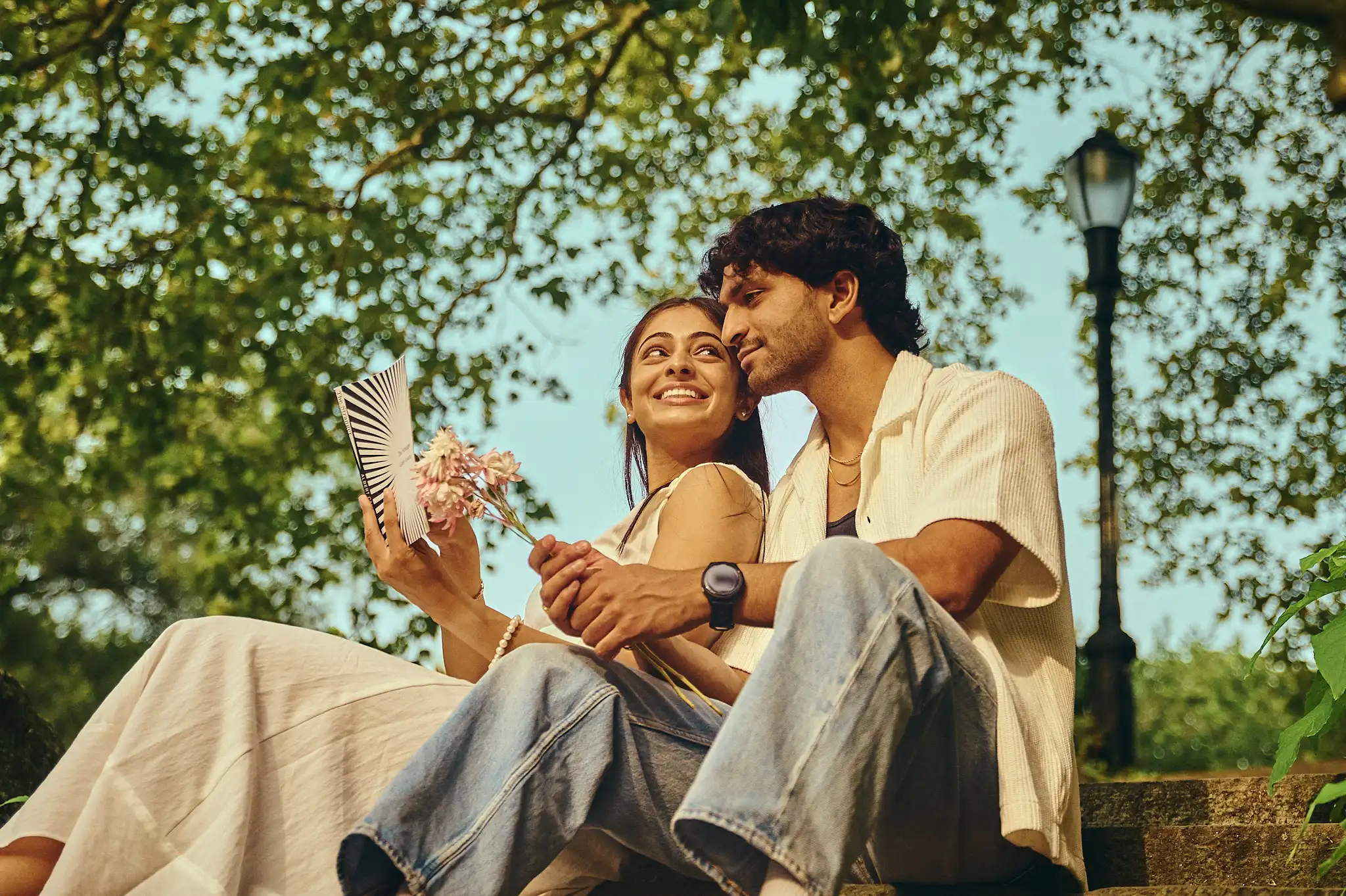 Couple beneath the Manhattan Bridge with golden underside lit by sunset and lush greenery