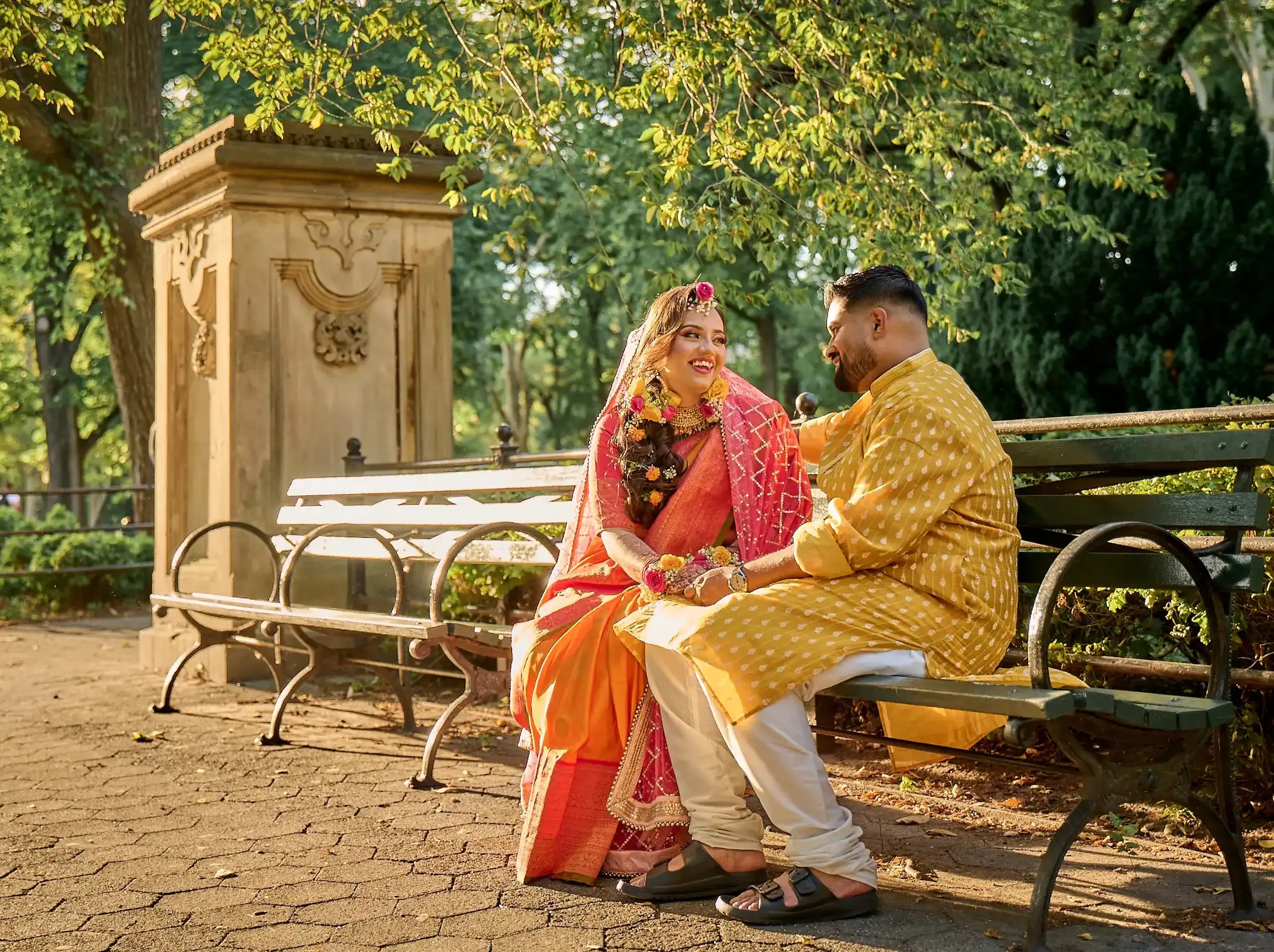 Aerial view of the Nikkah ceremony — bride in red and groom in navy on a patterned rug, separated by a floral garland, beneath a chandelier