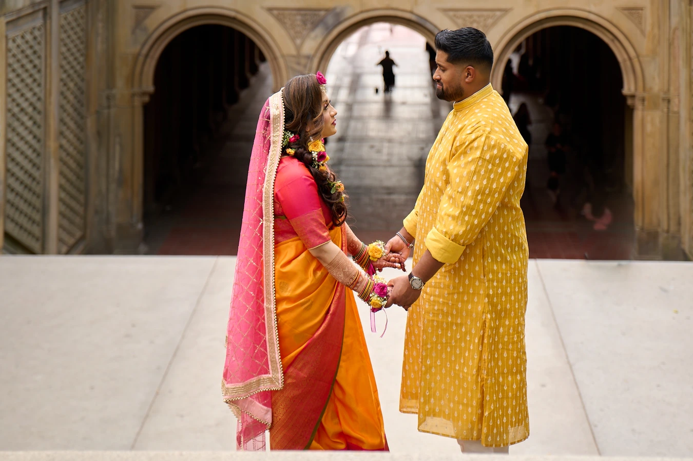 Couple in yellow and orange holding hands at the top of Bethesda Terrace's grand stone arches