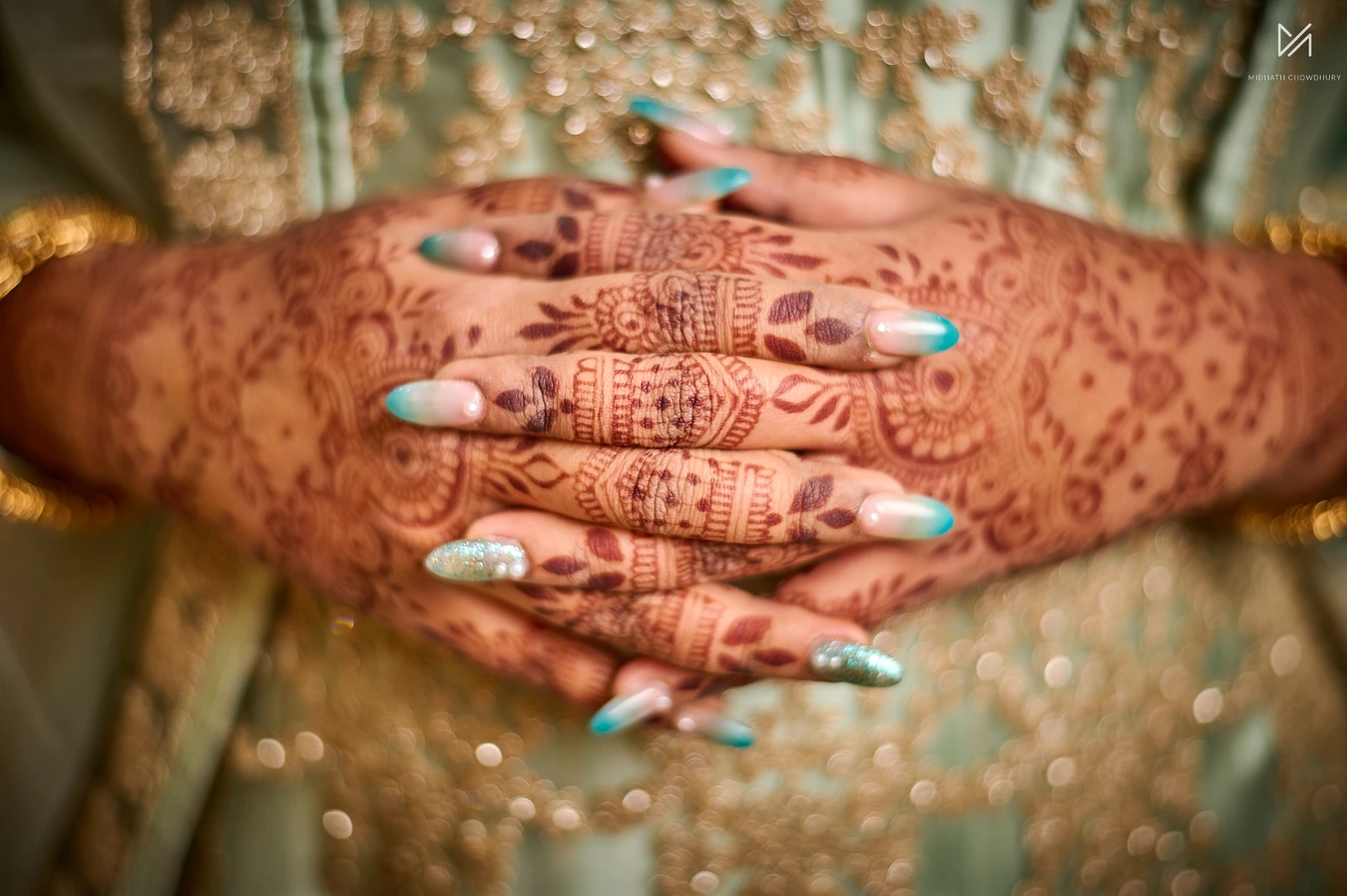 Close-up of bride's stacked hands with intricate red mehendi henna patterns and teal nails