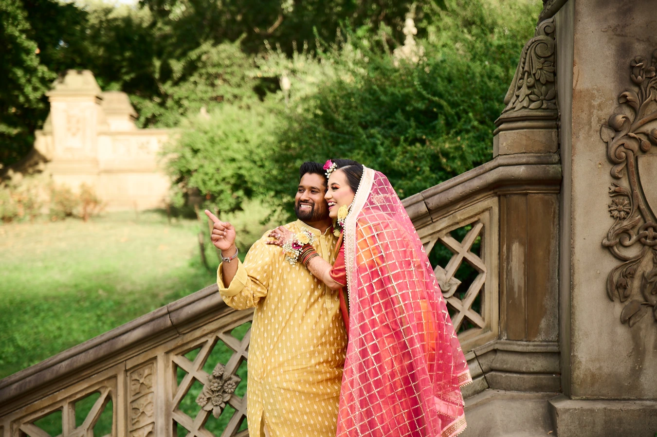 Couple looking off-frame together, groom pointing, ornate carved stone railing beside them
